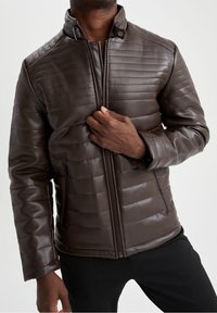 Giacca marrone in ecopelle con trama trapuntata, collo alto, cerniera frontale e tasche laterali. Progettata per un look moderno e casual.