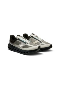 Chaussures de sport grises et noires avec une tige en mesh, un design à motifs et une semelle rembourrée dotée de pochettes d'air visibles. Lacets blancs avec des accents bleus.
