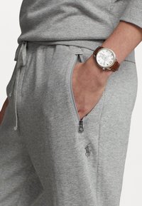 Grå sweatshirt i mjukt tyg med långa ärmar, med en ficka med dragkedja och en broderad logotyp. Brun klocka med läderrem.