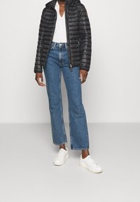 Czarna pikowana kurtka z kapturem, w połączeniu z jasnoszarą koszulką z dekoltem w serek, szerokimi niebieskimi dżinsami i białymi trampkami.