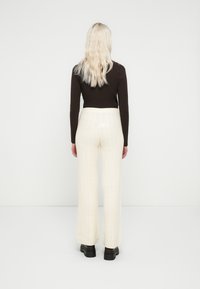 Pantaloni crem cu model tricotat în formă de cablu, cu design cu picioare largi, talie înaltă și model texturat. Asortați cu un top închis la culoare, mulat, și pantofi negri.