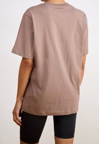 Brun bomulls-t-shirt med korta ärmar, rund halsringning och avslappnad passform. Bärs med svarta cykelbyxor.