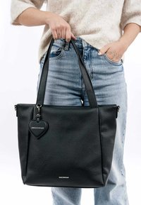 Sac fourre-tout en cuir noir avec une finition texturée, doté de deux longues poignées et d'une étiquette en forme de cœur. Fermeture zippée sur le dessus.