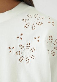 Hvit bomullsbluse med blomsterbroderi og utskjæringer. En enkel design med myk tekstur og rund halslinning.
