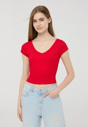 Top corto a righe rosso con maniche corte e scollatura a V profonda, abbinato a jeans azzurri strappati, che mostrano una silhouette aderente.