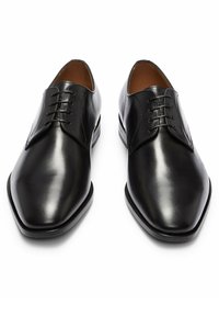 Paire de chaussures habillées en cuir noir brillant avec laçage fermé et bouts carrés arrondis, présentée côte à côte sur un fond blanc.