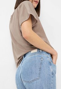 Un haut marron à manches courtes associé à un jean bleu clair. Le haut a une texture lisse ; le jean présente une coupe classique et des poches.