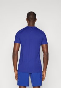 Niebieska koszulka sportowa z okrągłym dekoltem, krótkimi rękawami i małym logo na plecach, wykonana z lekkiego, gładkiego materiału.