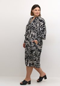 Robe à motif tourbillon noir et blanc avec une coupe ample, des manches longues et une poche. Accentuée par un poignet texturé contrastant.