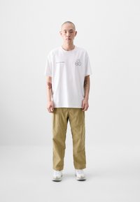 White cotton t-shirt featuring a graphic with hexagonal elements and text. Paired with beige cargo pants and white athletic shoes.
