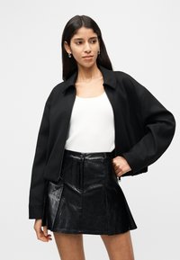 Μαύρο cropped bomber μπουφάν με εμπρόσθιο φερμουάρ, σε συνδυασμό με λευκή ριμπ μπλούζα και μαύρη μίνι φούστα από ψεύτικο δέρμα με πιέτες.
