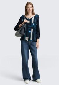 Flerfärgad blus med geometriskt mönster, marinblå ärmar, kombinerad med vida blå jeans och vita sneakers. Svart handväska ingår.