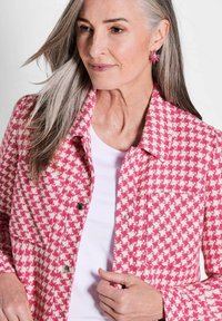 Roze en crèmekleurige houndstooth jas met een ontspannen pasvorm, voorzakken en drukknoopsluitingen. Witte shirt eronder, gladde, textuurstof.