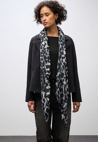 Leopardmönstrad scarf i svart och grått, lättviktig tyg, hänger mjukt. Bärs med en svart topp och en mörk jacka, vilket skapar kontrast.