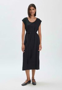 Mustat hihattomat mekko, jossa on kuppikaula-aukko, vyötärövyö ja sivurei'itykset. Valmistettu pehmeästä kankaasta ja rennosta leikkauksesta, ulottuen polven keskelle.