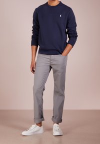 Marinblå sweatshirt med rund hals och påsytt logotyp, i kombination med grå chinos med upprullad nederkant och vita sneakers. Slät tyg, avslappnad passform.