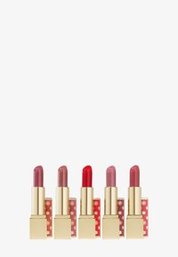 Cinque rossetti Estée Lauder in diverse tonalità di rosa e rosso, con astucci dorati e decorazioni festose in rosso e oro.