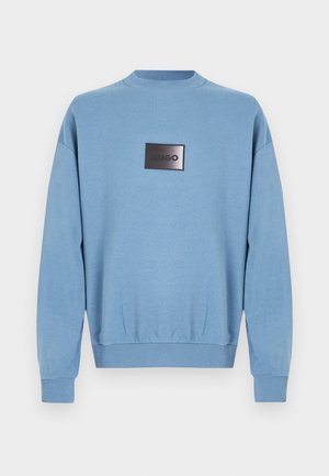 Hele sinine pikkade varrukatega dressipluus soonikkoega krae, varrukaotsad ja alumine serv, mille keskel on must ristkülikukujuline plaastriga, millel on tekst "HUGO".