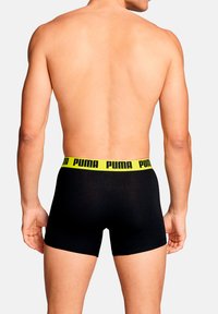 Schwarze Boxershorts mit einem breiten, leuchtend gelben Bund mit dem "PUMA"-Logo, die ein figurbetontes Design und eine glatte Textur zeigen.