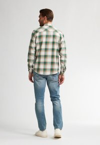 Geruite flanellen blouse in crèmekleuren met groen- en blauwtinten, gecombineerd met lichtblauwe spijkerbroek. Heeft lange mouwen en een standaard kraagontwerp.