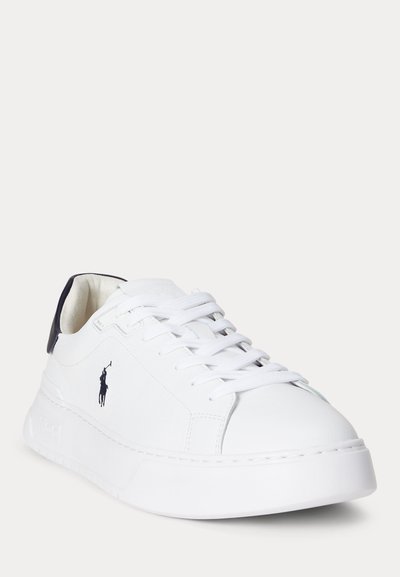 Balts ādas krosenis ar biezām zolēm, baltām auklām, tumši zilu papēža cilpu un melnu izšūtu polo spēlētāja logo sānos.