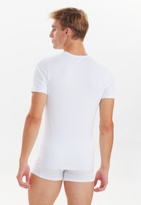 White short-sleeve fitted t-shirt made of smooth fabric, paired with white boxer briefs, viewed from the back.