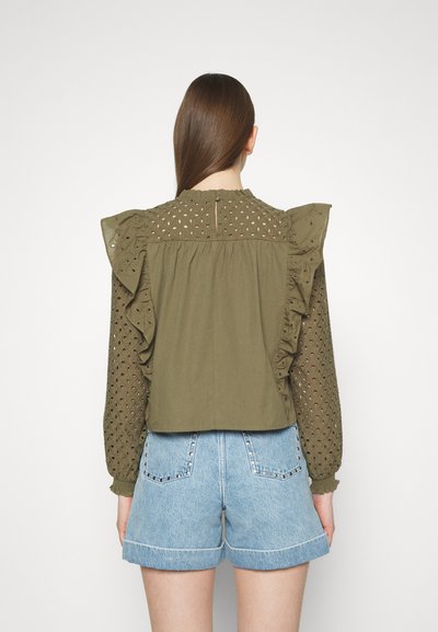 Blouse vert olive avec des manches à volants, détails en œillet et dos en trou de serrure, associée à un short en jean bleu clair avec des accents cloutés.