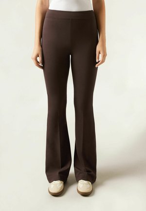 Pantalons marron évasés en tissu extensible, avec une texture lisse et une taille haute, associés à des baskets beige.