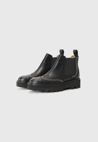 Botas Chelsea de cuero negro con tachuelas decorativas de plata, paneles laterales elásticos y suelas de goma resistentes. Altura de tobillo clásica y acabado suave.