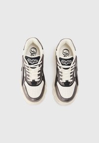 Duté tenisky s lesklým černým a šedým svrškem, krémovými akcenty a silnými bílými podrážkami. Mezi vlastnosti patří perforovaný špička a bílé tkaničky.