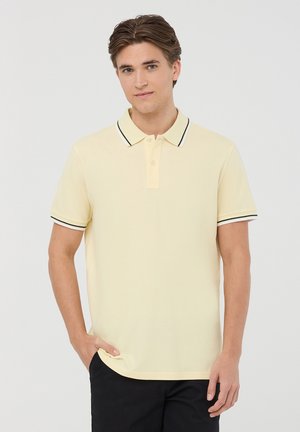 Polo shirt giallo chiaro in cotone con vestibilità rilassata, caratterizzato da un colletto a righe nere e bianche e maniche corte.