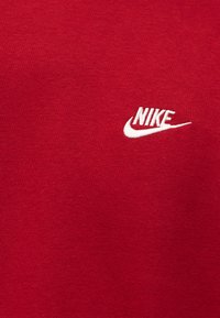 Κόκκινο ύφασμα με μικρό λευκό λογότυπο Nike κεντημένο στη δεξιά πλευρά.