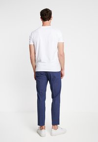 Vit kortärmad t-shirt i kombination med blå skräddarsydda byxor och vita sneakers. Synlig sömnad på båda plaggen. Enkelt design, inga mönster.