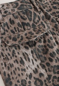 Kordstoff mit Leopardenmuster, bestehend aus einem braunen und schwarzen Muster mit vertikalen Rippen; enthält eine flache Tasche und kontrastierende Nähte.