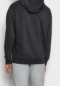 Kolgrå hoodie med en mjuk textur, justerbar dragsko och ribbad nederkant. Bärs tillsammans med ljusgrå sweatpants.