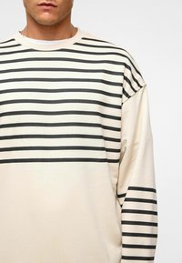 Beige sweatshirt met verticale zwarte strepen, ronde hals en verlaagde schouders. Zachte textuur, casual ontwerp en een relaxte pasvorm.