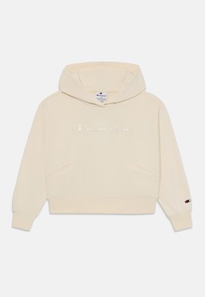 Sudadera crema con bolsillo canguro, que presenta un logotipo bordado de "Champion" y un pequeño parche de logo en la manga. Material suave, diseño casual.