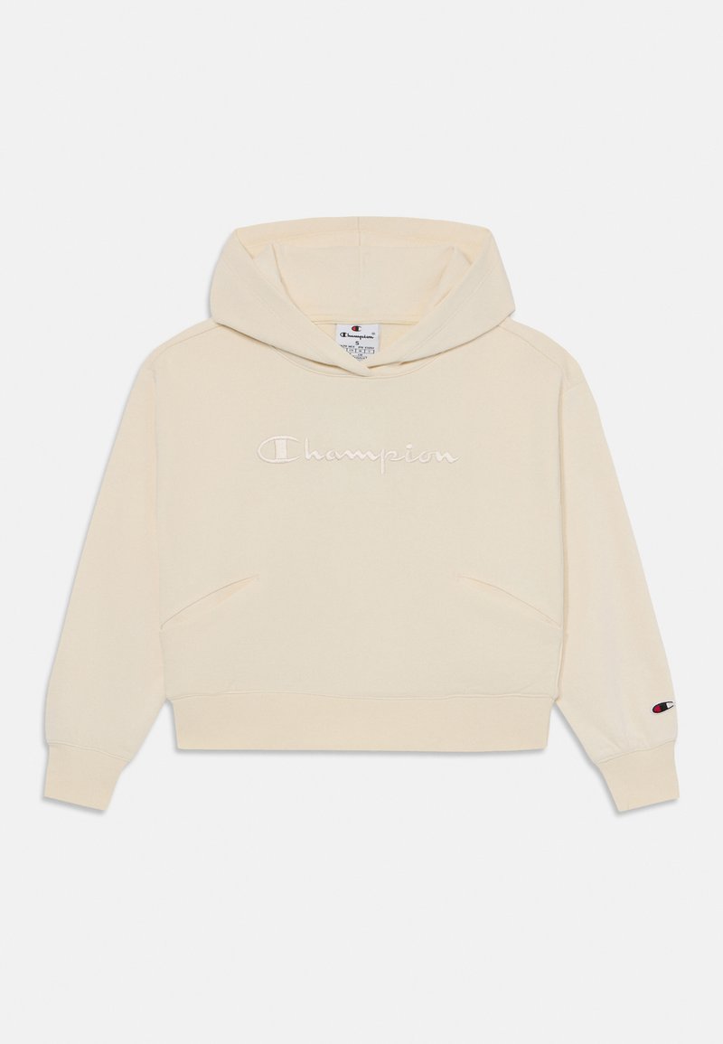 Sudadera crema con bolsillo canguro, que presenta un logotipo bordado de "Champion" y un pequeño parche de logo en la manga. Material suave, diseño casual.