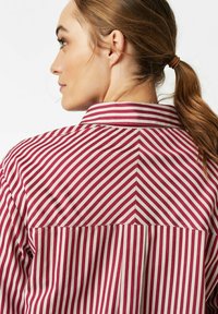 Red and white striped shirt with a collared neckline, featuring a back yoke seam and smooth fabric texture.