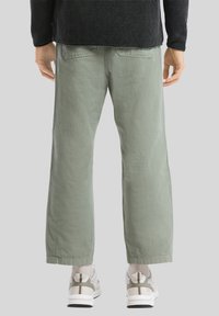 Pantalons larges vert clair avec une texture lisse, poches arrière et coupe droite, associés à des baskets blanches et grises.