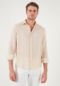 Camisa de botones a rayas beige con mangas largas arremangadas, hecha de tela ligera, con un clásico cuello y un dobladillo curvado.