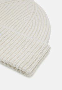 Cream ribbed knit beanie featuring a folded cuff. Made of soft wool-like material with a textured finish. Simple and functional design.