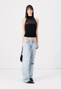 Black halter top with sheer paneling, paired with light blue distressed jeans and black pointed-toe shoes. Small black handbag slung over shoulder.