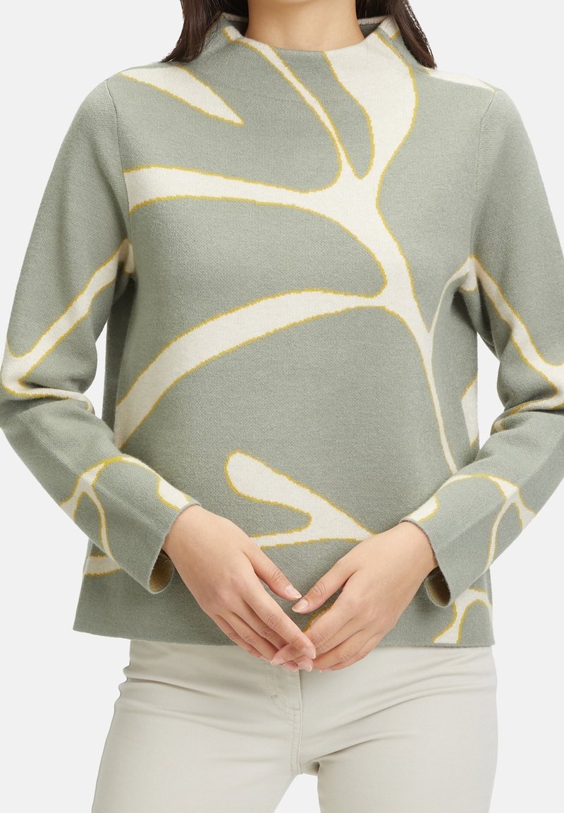 Pull vert clair en matériau doux, doté de motifs abstraits de feuilles en blanc et jaune, avec un col montant et des manches longues.