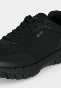 Μαύρο sneaker BOSS με υφή υφάσματος, ελαστική σόλα, χρωματιστά κορδόνια και λογότυπο στη πλευρά και τη γλώσσα, γωνιακά ώστε να εμφανίζονται λεπτομέρειες από μπροστά και πλάι.