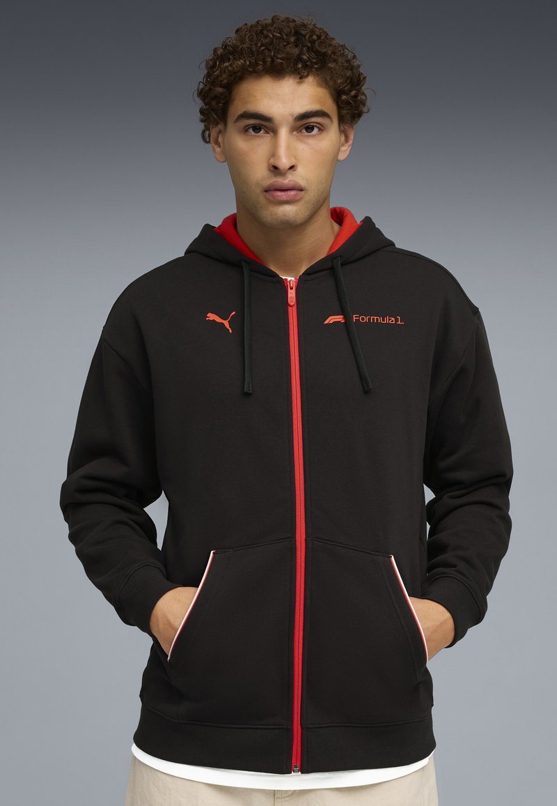 Sudadera negra con acentos rojos y logo de Fórmula 1. Presenta un cierre de cremallera, bolsillos tipo canguro y una capucha interna en contraste.