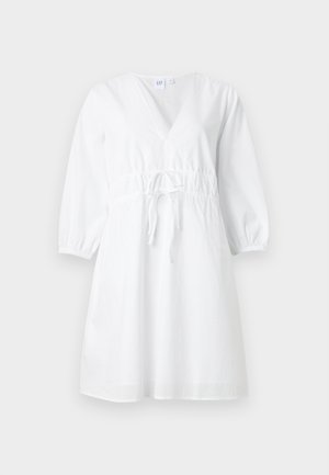 Valge põlvpikkusega kleit V-kaelusega, pikkade volangiliste varrukatega ja kogutud vööpaelaga ühtlasel taustal.