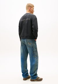Tmavohnedá mikina s logom "Tommy Jeans" na chrbte, skombinovaná so svetlomodrými džínsovými cargo nohavicami so vreckami a prešívaním.