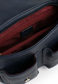 Interno della borsa in pelle blu navy con foderatura borgogna, dotato di diverse tasche con zip e chiusura a pulsante magnetico. Texture liscia.