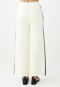 Wijde broek in romig witte stof met zwarte zijstrepen en een gladde textuur. Ontworpen met een hoge taille en een relaxte pasvorm.